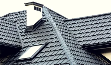 House roof with black metal tiles, a skylight window, and a white chimney.