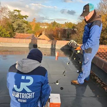 Two workers on a flat roof inspecting or installing equipment, one holding a string of lights.