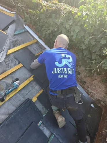 Worker in blue JustRight Roofing shirt installing roof tiles on a sloped roof.