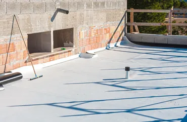 Flat rooftop with fresh white waterproof coating drying in the sun under a wall and railing.