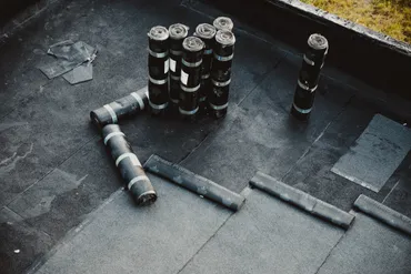 Rolled roofing materials arranged on a flat roof under construction near a grassy edge.