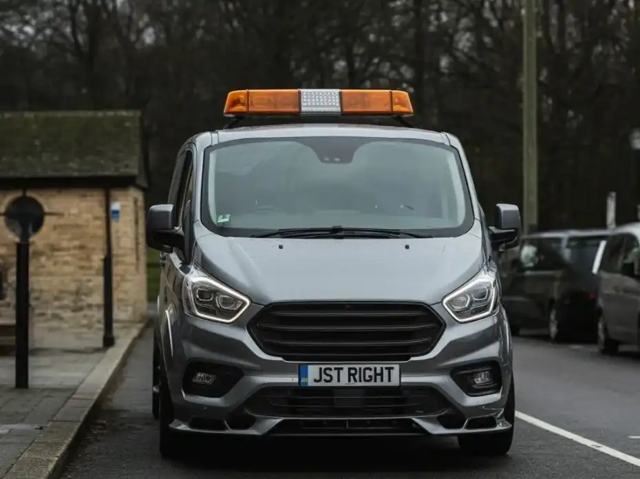Front view of gray van with an orange emergency lightbar on top and license plate reading JST RIGHT.