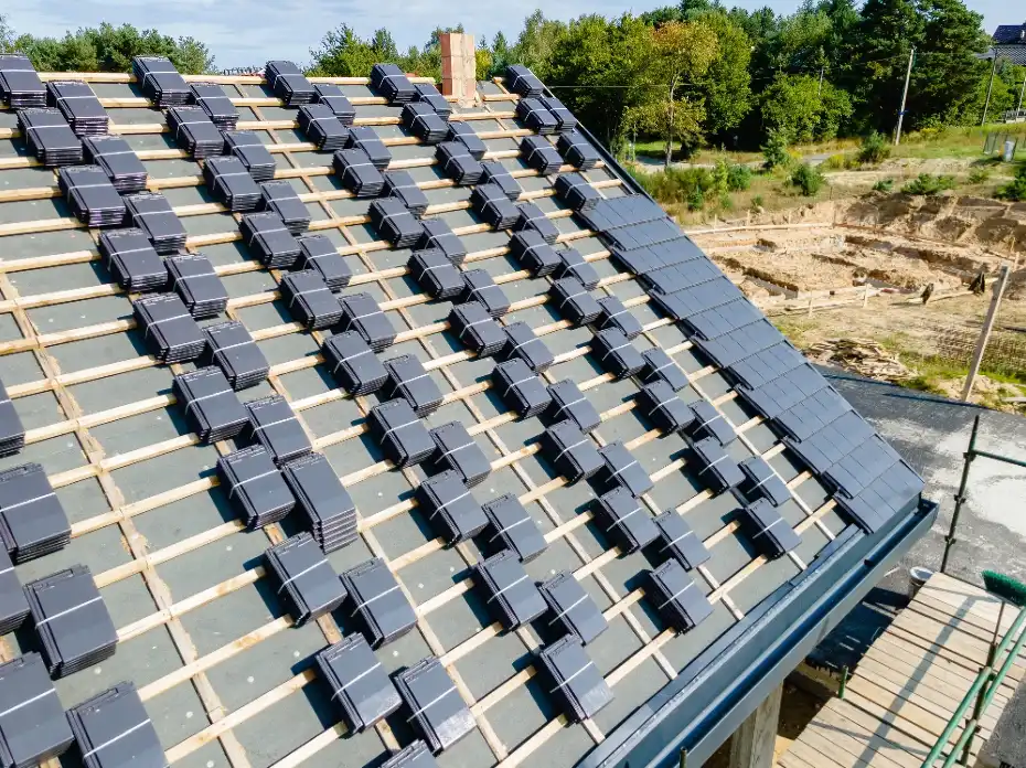 Partially tiled roof with stacked dark tiles aligned on wooden battens for installation.